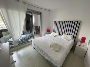 Ein Schlafzimmer mit einem großen Bett, einer Schiebetür zu einem Balkon, einem gestreiften Kopfteil und zwei Nachttischen mit roten Lampen.