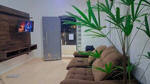 Un salon équipé d’un téléviseur à écran plat, d’un canapé, d’une grande plante et d’une porte donnant sur une autre pièce.