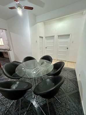 A dining area with a glass table surrounded by black chairs, a ceiling fan, and patterned floor tiles.