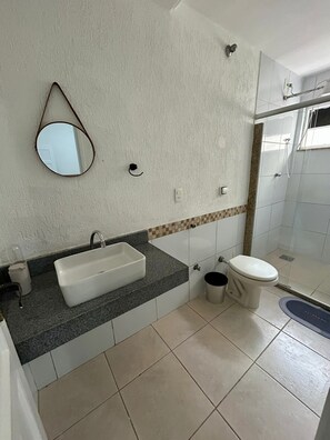 Une salle de bain avec un lavabo rectangulaire, des toilettes, une douche et un miroir au mur.