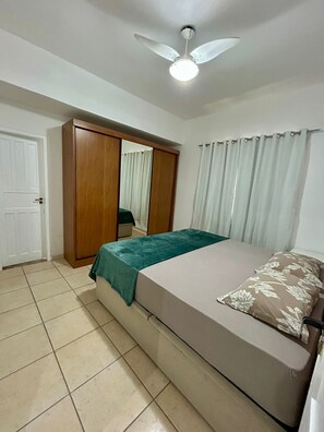 Une chambre à coucher comprenant un lit, une armoire, un ventilateur de plafond et une fenêtre avec des rideaux.