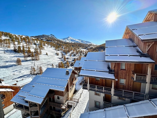 Ein verschneites Bergdorf mit Holzhäusern und einer Skipiste im Hintergrund.