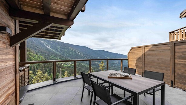 Un balcon en bois, agrémenté d’une table et de chaises, qui offre une vue sur un paysage montagneux.