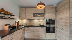 Une cuisine moderne avec des armoires en bois, un plan de travail noir, un four encastré et un luminaire suspendu.
