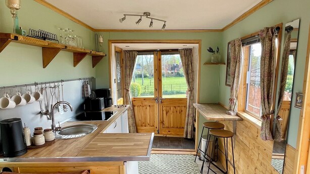 Una cocina con gabinetes de madera, un lavamanos, una cafetera y una ventana con cortinas.