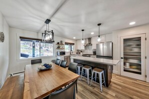 A modern kitchen with a wooden dining table, bar stools, and a large window. - 4 Bedrooms, Lakeviews, Hot Tub, Pool Table! (South Lake Tahoe)