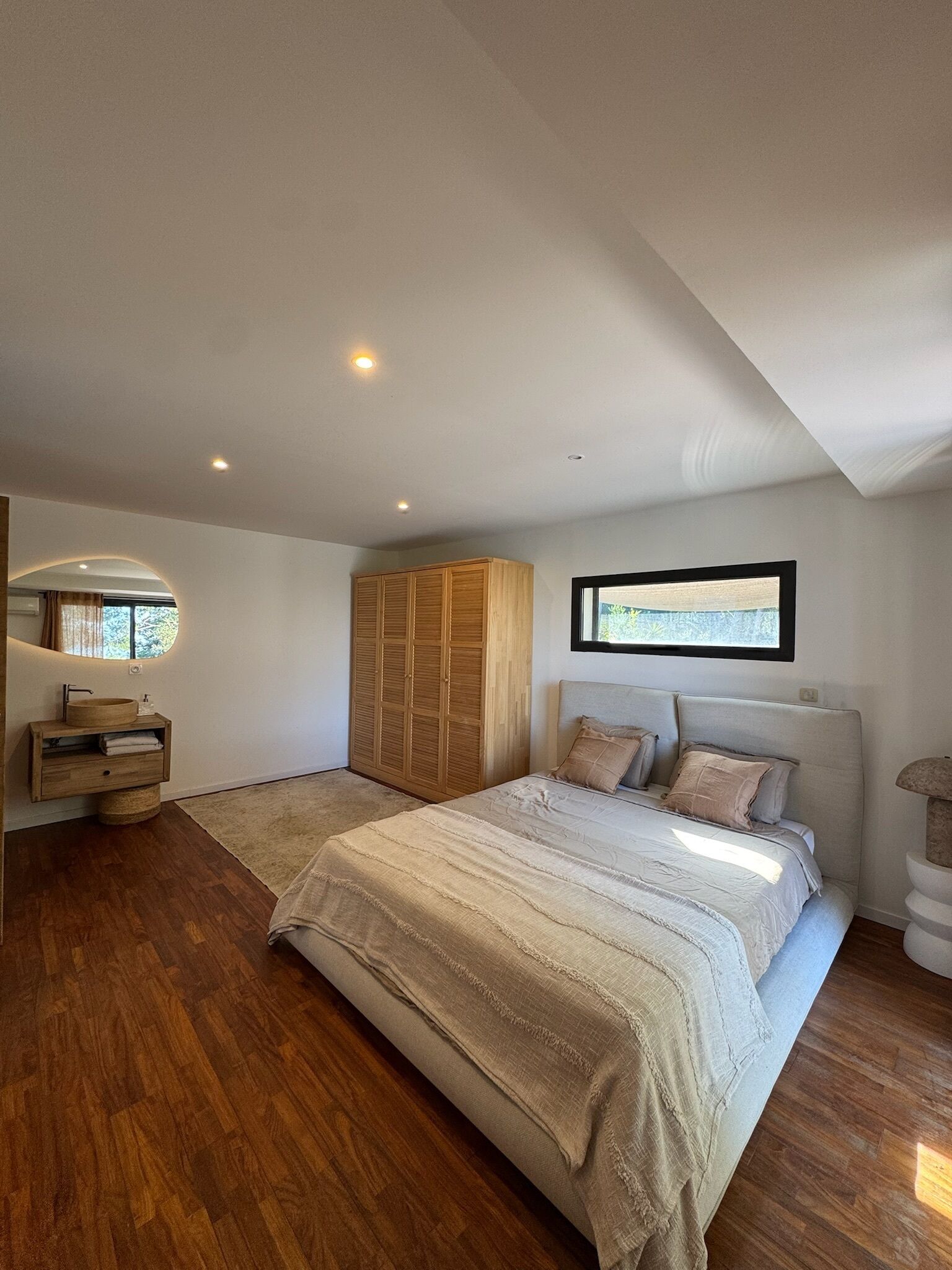 Een slaapkamer met een groot bed, een houten garderobe en een ronde spiegel.