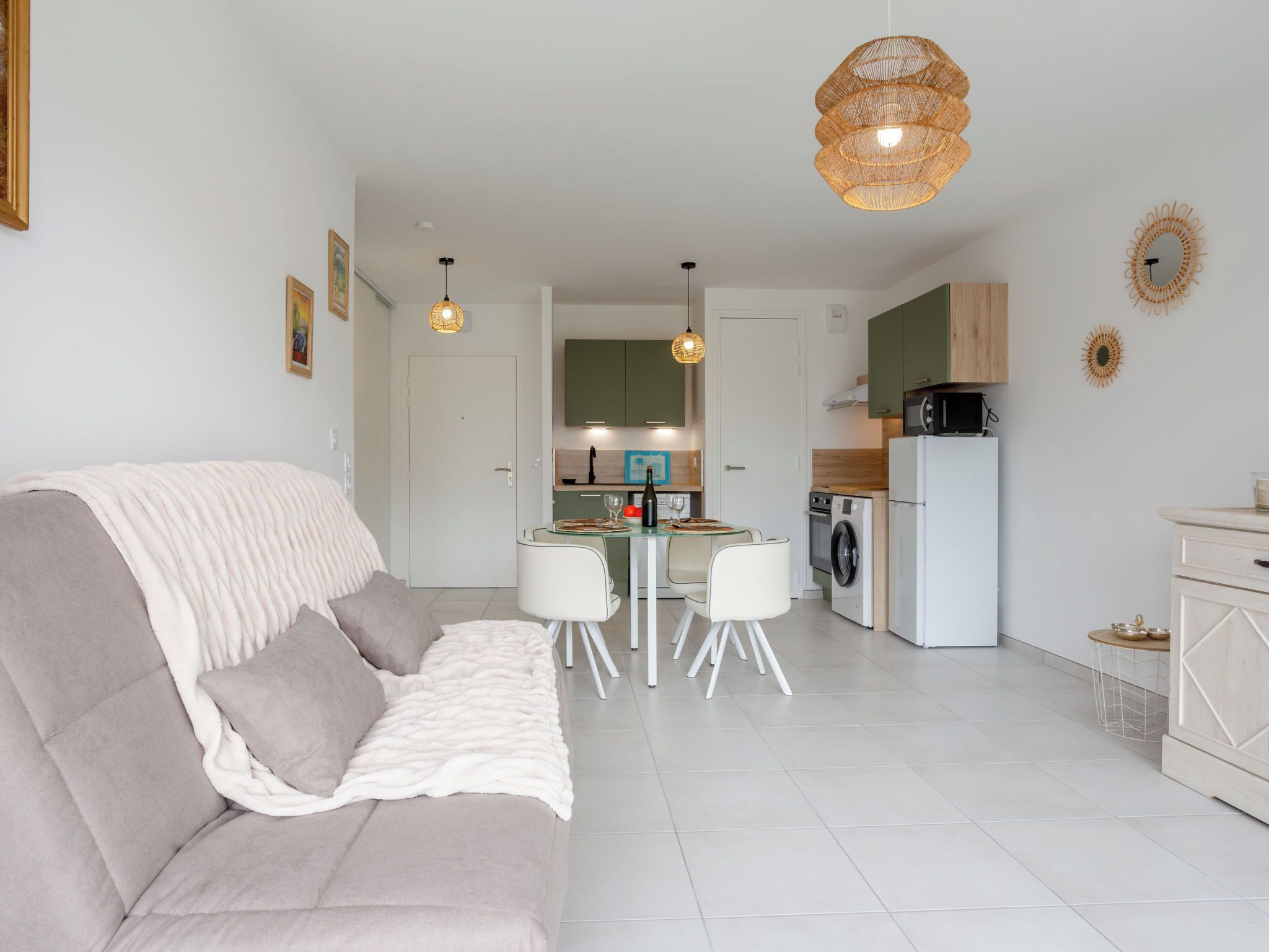 A modern living room with a sofa, a dining table with chairs, a kitchen area with appliances, and a hanging light fixture.