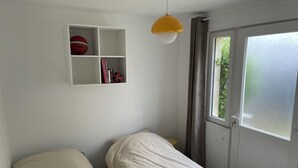 Een kamer met twee bedden, een witte plank met boeken en een basketbal, een gele hanglamp, en een raam met uitzicht op groen.