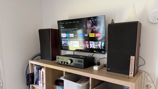 Een televisie op een houten standaard met speakers, een boekenkast en opbergbakken.