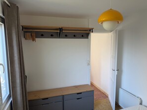 A bedroom with a wooden bed frame, a grey dresser, a wooden shelf, a white door, and a yellow pendant light. - Charming house facing the Atlantic, garden and pergola 2 min from beaches (Fouras)