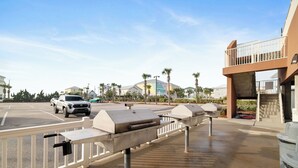 Uma área de estacionamento com churrasqueiras, uma caminhonete branca e um edifício de vários andares com varandas.