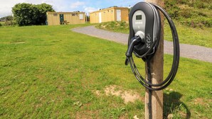 Una stazione di ricarica per veicoli elettrici in un’area verde con un sentiero che conduce a un edificio.
