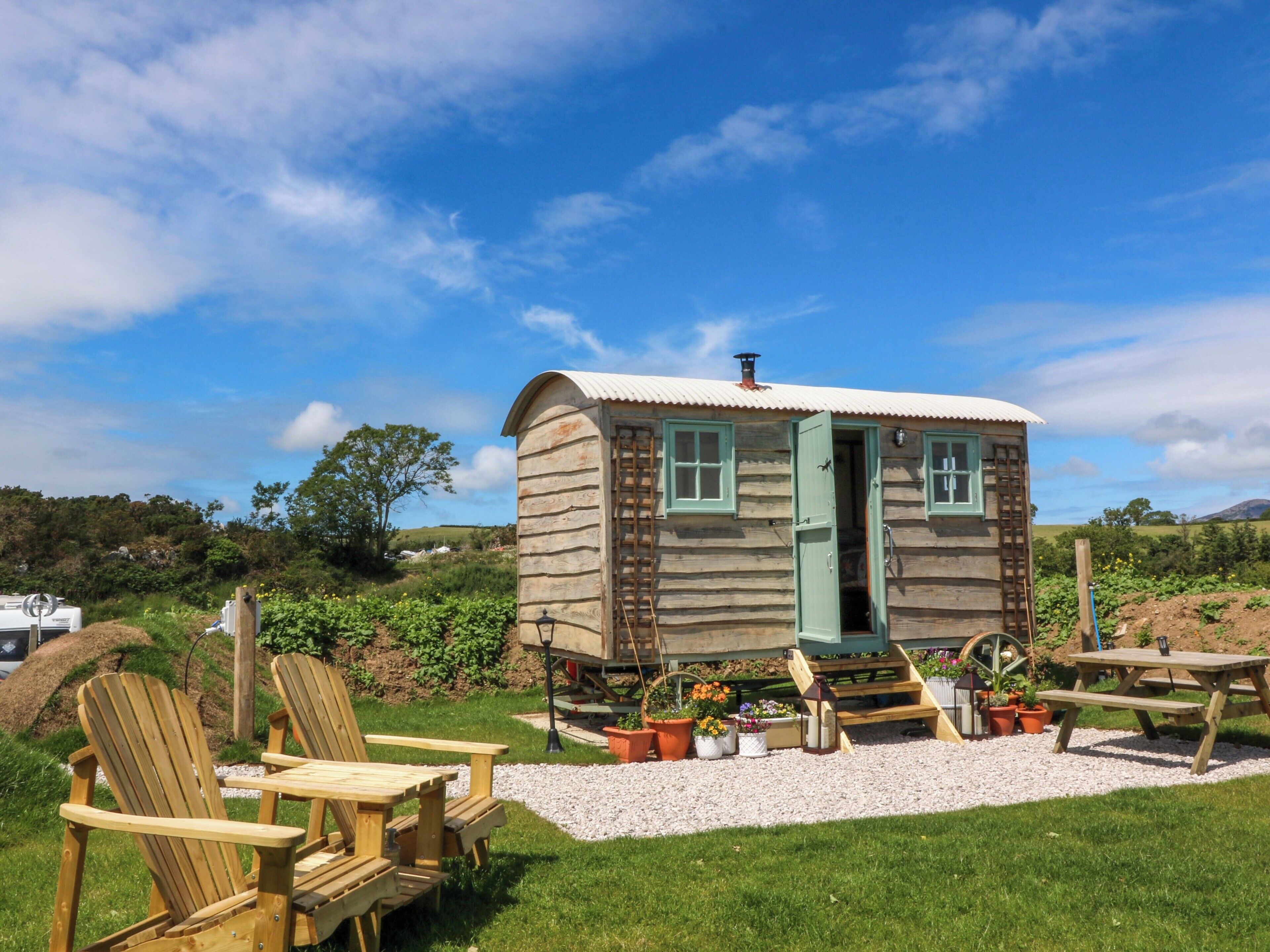 A wooden cabin with a door, windows, and a wheelhouse. There are wooden chairs and a picnic table outside.