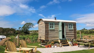 A wooden cabin with a door, windows, and a wheelhouse. There are wooden chairs and a picnic table outside.