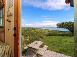 Puerta de madera que da a un patio con mesa y banco, con vistas a un paisaje costero con campos y una masa de agua.