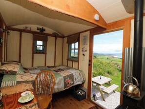A cozy room with a bed, a wooden chair, a table with a kettle, and a view of the countryside. - Cwt Bugail (Pwllheli)