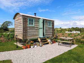 Eine Holzhütte mit Tür, Fenstern, einer kleinen Veranda und einem Kiesweg, der zu einem Picknicktisch führt.