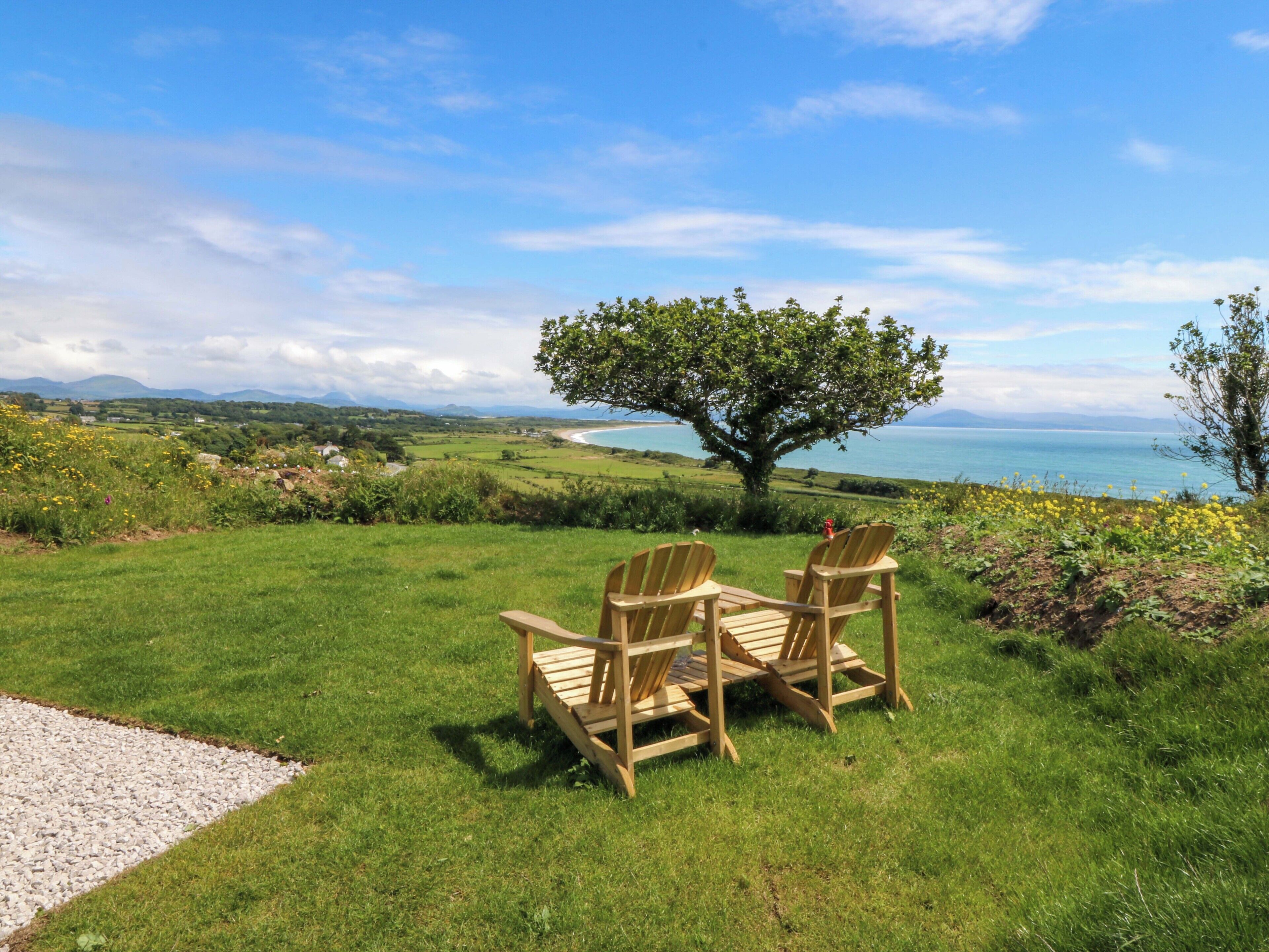 Zona verde con dos sillas de madera orientadas hacia un árbol y vistas al mar.