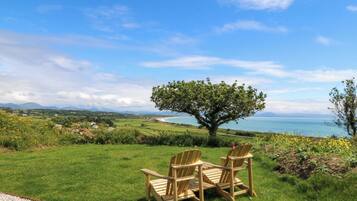 Zona verde con dos sillas de madera orientadas hacia un árbol y vistas al mar.