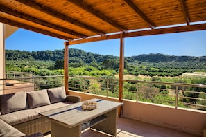 Ein Balkon mit einer Rattan-Sofa und einem Tisch, mit Blick auf eine üppige Landschaft.
