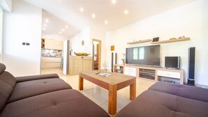 Una sala de estar moderna con un conjunto de sofá, una mesa de centro de madera, un televisor y una cocina al fondo.