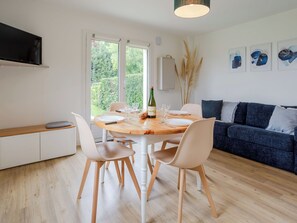 Ein moderner Essbereich mit Holztisch, weißen Stühlen, einer Couch und einem an der Wand montierten Fernseher.