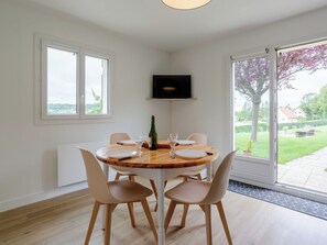 A dining area with a round table, four chairs, a bottle of wine, and a TV mounted on the wall. - Les Ducs de Normandie by Interhome (Houlgate)