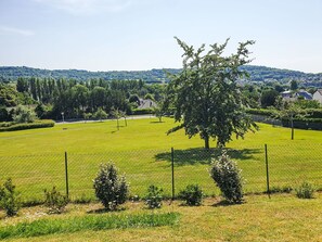 A fenced park with a large tree, a clear sky, and distant hills. - Les Ducs de Normandie by Interhome (Houlgate)