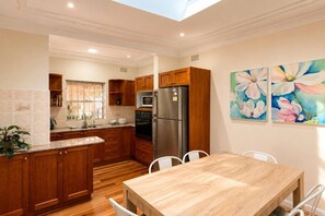 A kitchen with wooden cabinets, a stainless steel refrigerator, and a dining table with chairs. - 3BR Mascot House | 3 Queen Beds | Walk to Station (Mascot)