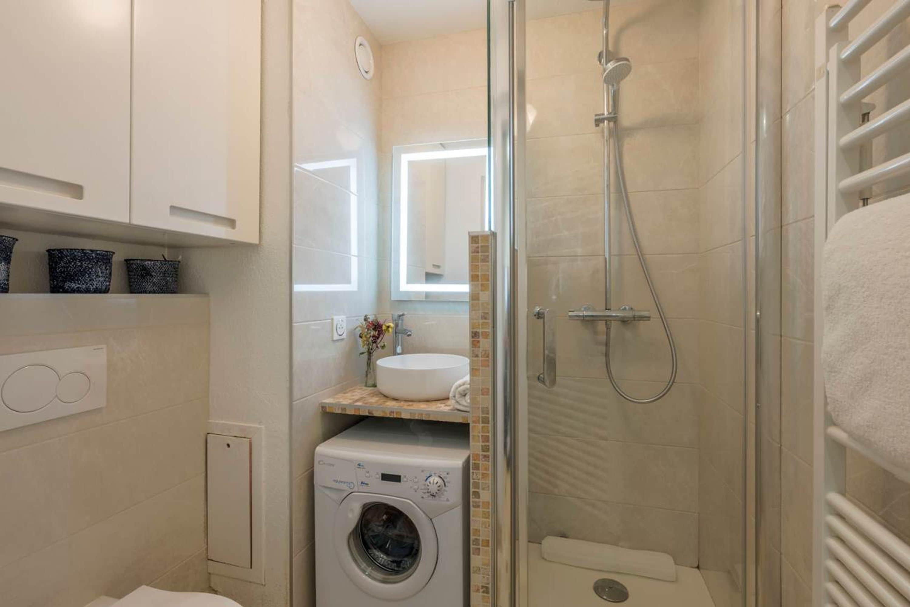 Un baño pequeño con lavadora, lavamanos con espejo y cabina de ducha.