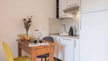 Una cocina compacta con armarios blancos, una cafetera y una cesta de frutas en la encimera.