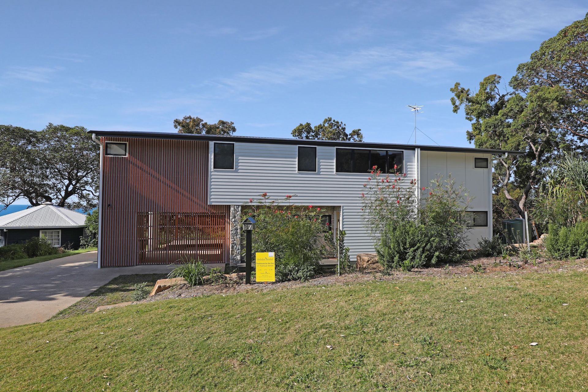 A modern two-story house with a flat roof, a fenced yard, and a clear sky.