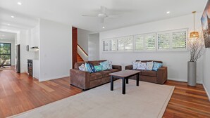 Ein modernes Wohnzimmer mit einer braunen Sofagarnitur, einem Couchtisch und einem großen Fenster mit Jalousien.