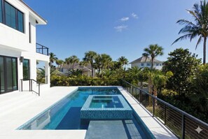 Ein modernes Haus mit Swimmingpool, umgeben von Palmen und blauem Himmel.