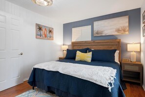 Un dormitorio con una cama, dos mesitas de noche, una puerta blanca y dos cuadros colgados en la pared.