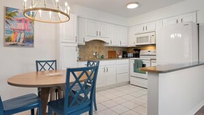Una cocina moderna con armarios blancos, una isla central y un área de comedor con sillas azules.