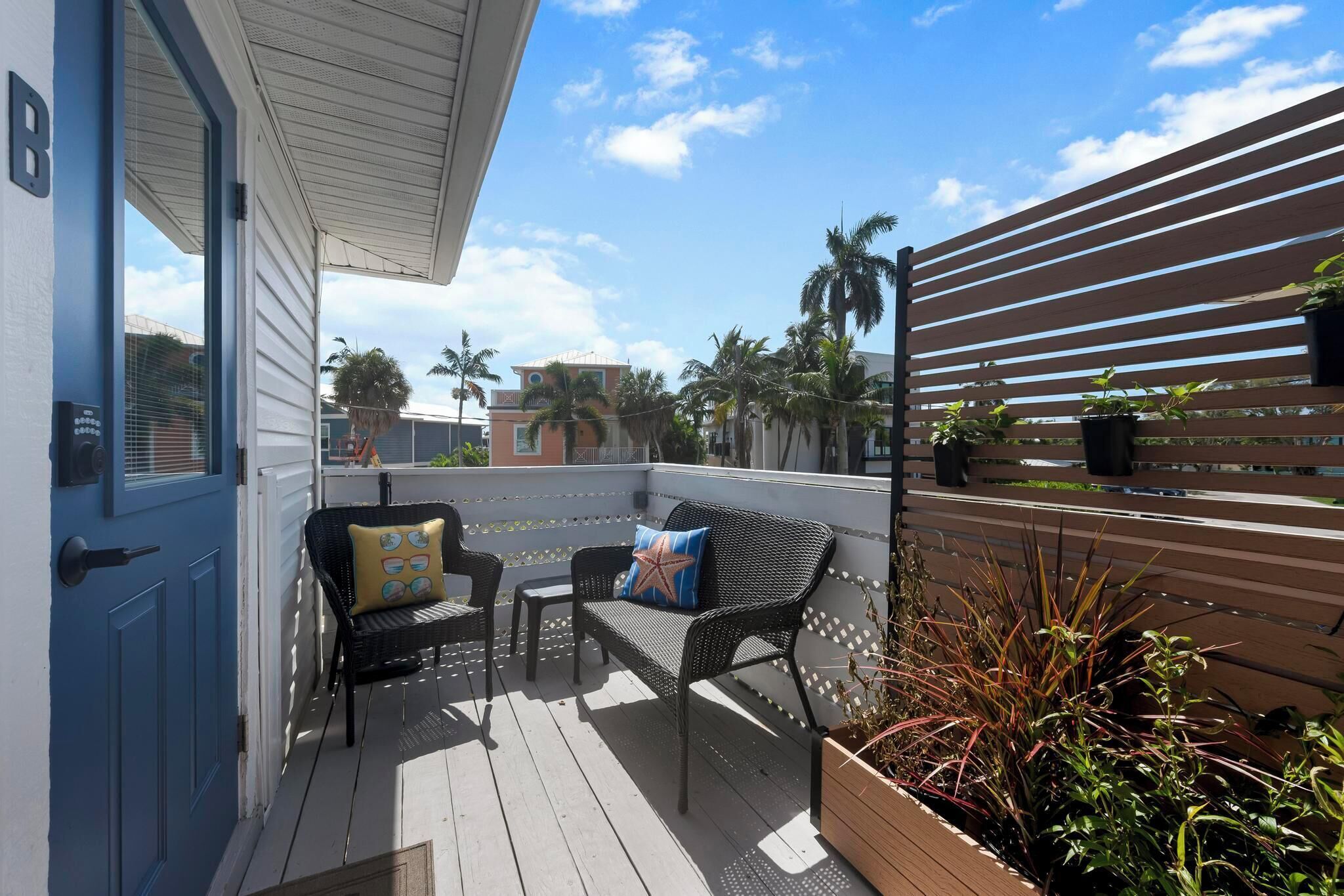 A covered outdoor seating area with two chairs and a bench, a wooden fence, and potted plants.