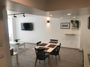 A modern dining area with a rectangular table, black chairs, recessed ceiling lighting, a mounted flat-screen TV, and a wall-mounted shelf with plants. - Oceanview Family Retreat in Vi a Laundry Parking (Vina del Mar)