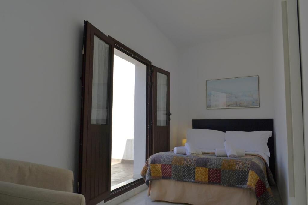 Un dormitorio con cama, una silla, un cuadro en la pared y una puerta que da a un espacio exterior.