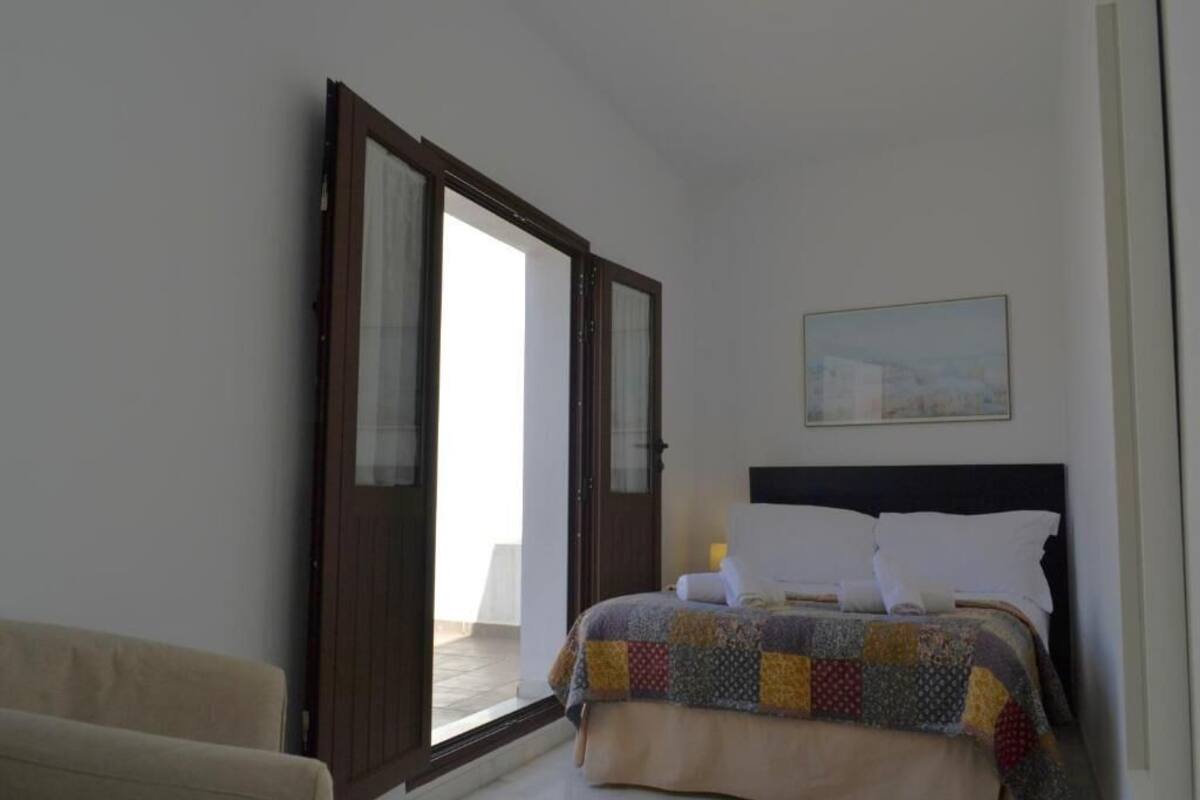 Un dormitorio con cama, una silla, un cuadro en la pared y una puerta que da a un espacio exterior.