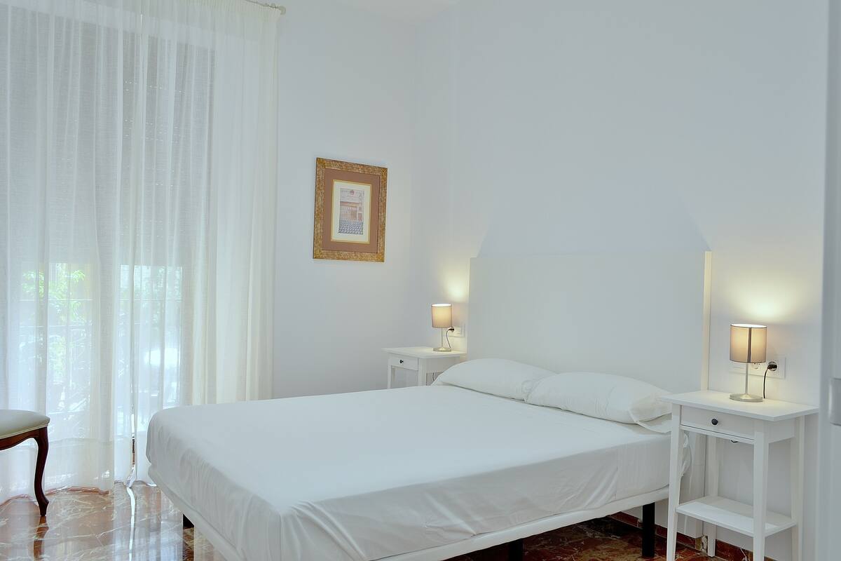 Un dormitorio con una cama, dos mesitas de noche, una silla y un cuadro en la pared.