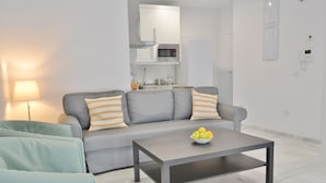 Ein modernes Wohnzimmer mit einem grauen Sofa, einem Couchtisch und einer Küchenzeile im Hintergrund.
