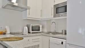Una cocina moderna con armarios blancos, microondas integrado, tostadora y lavavajillas.