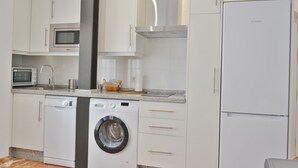 Eine moderne Küche mit weißen Schränken, integriertem Mikrowellenherd, Geschirrspüler, Waschmaschine und Kühlschrank.