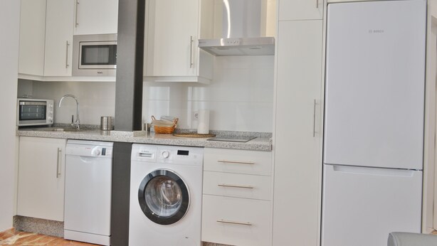 Una cocina moderna con armarios blancos, microondas integrado, lavavajillas, lavadora y refrigerador.