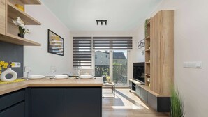 A modern kitchen with a central island, wooden shelves, and a dining area with a table set for two. - Modern Apartment with Parking | Balcony | Smart TV (Sosnowiec)