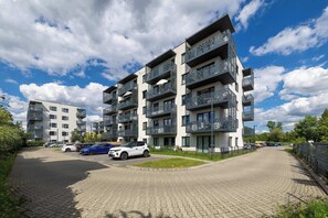 A multi-story residential building with balconies, a paved driveway, and parked cars.