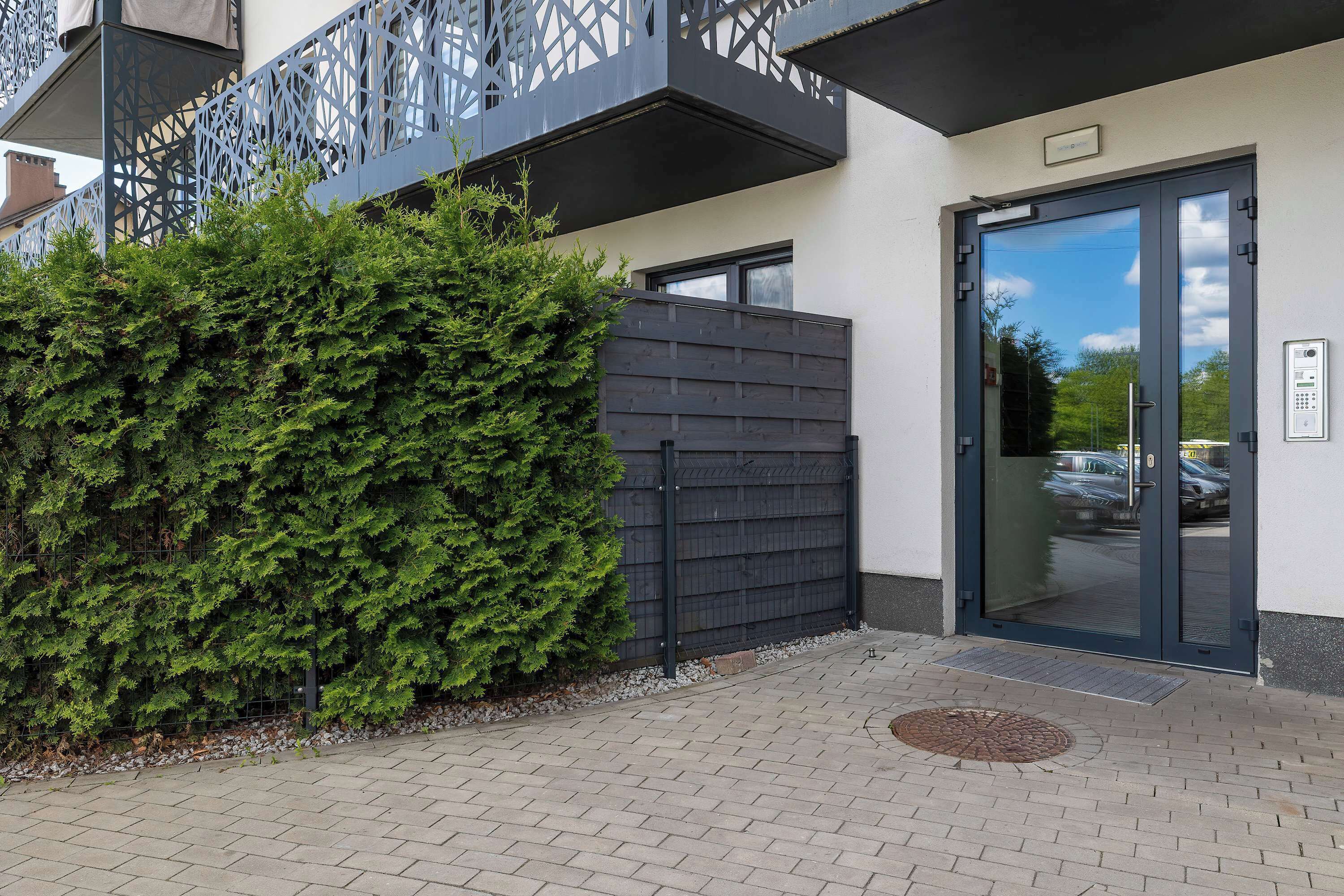 Een gevel met een zwart hek, een metalen balkon en een deur met een codeerapparaat.
