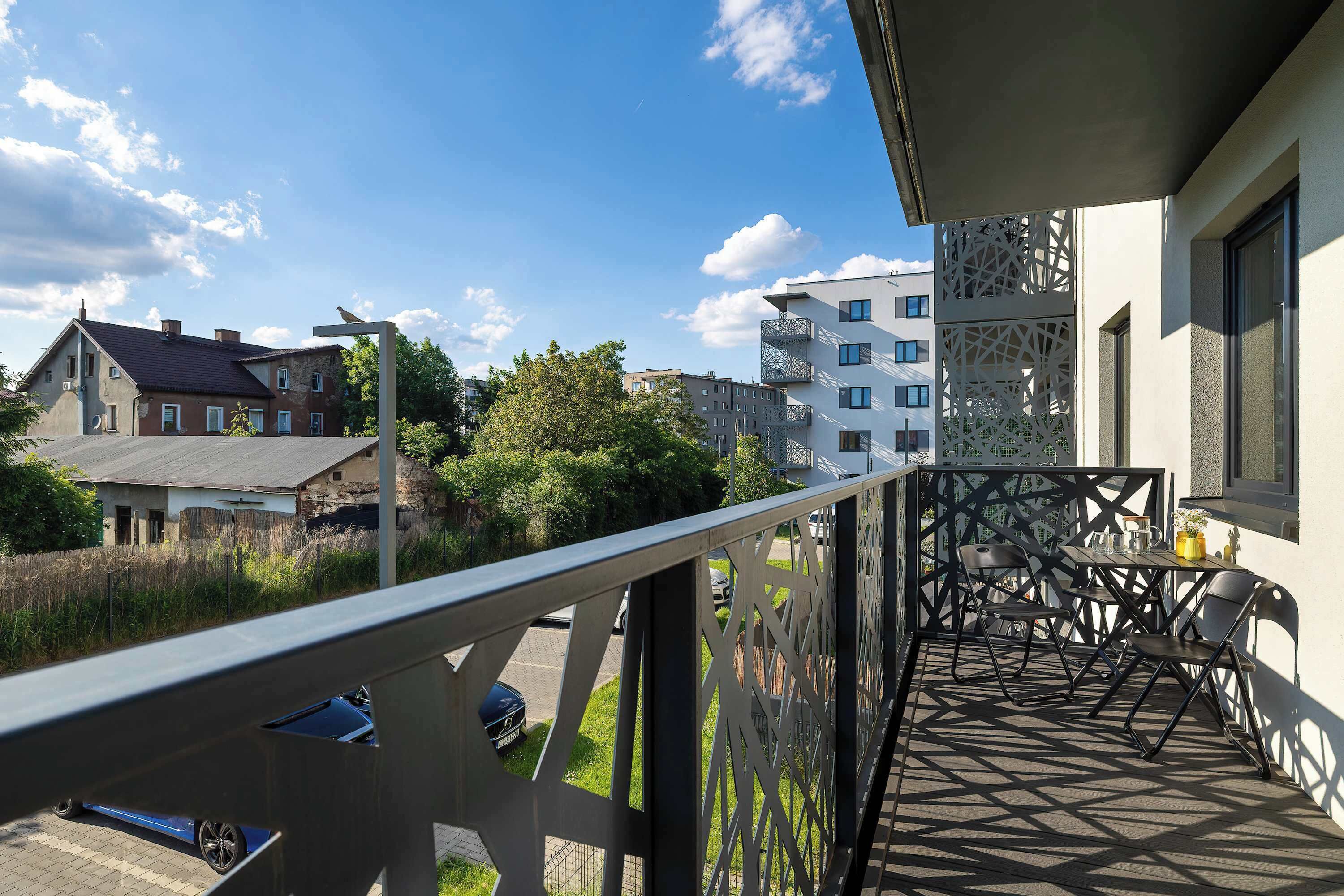 A balcony with a table and chairs, a railing, and a view of buildings and greenery.